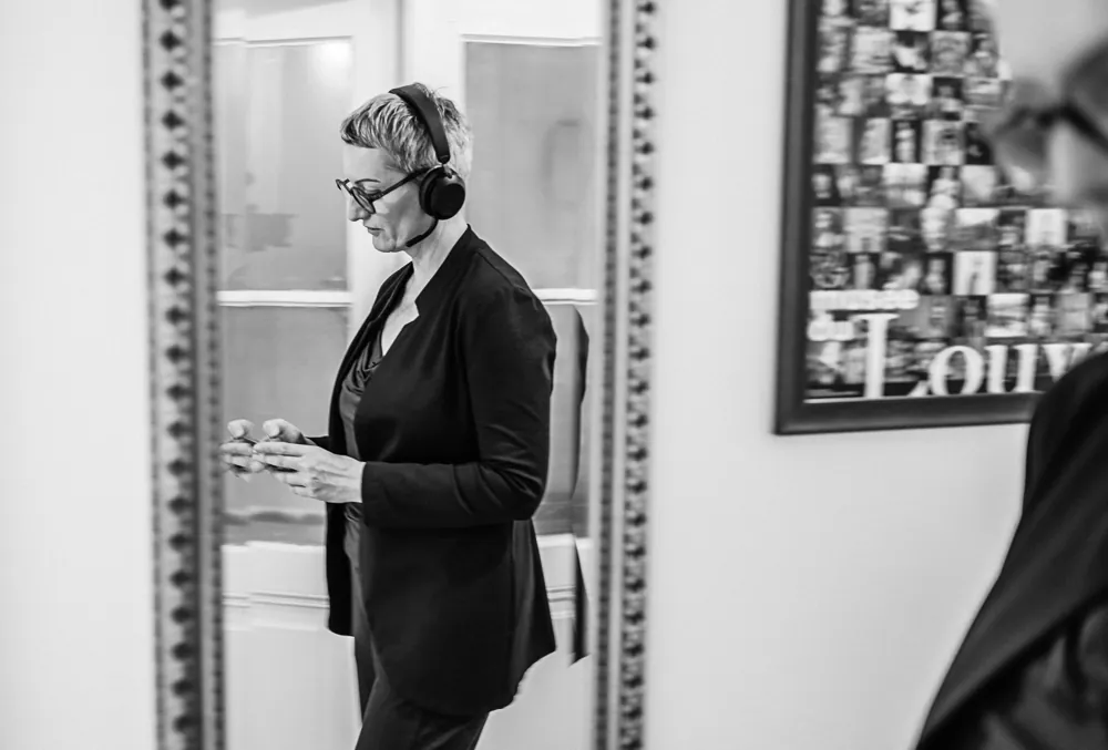 Daniela Krainčić mit Headset vor einem Spiegel, daneben ein Plakat des Louvre