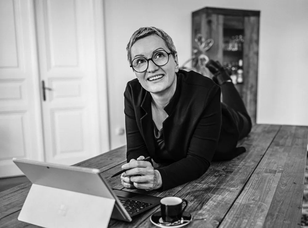 Daniela Krainčić liegt auf einem Holztisch vor ihrem Laptop und blickt lächelnd nach oben